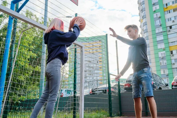 Teenagers guy and girl on an outdoor basketball court playing street basketball — Stock Photo, Image