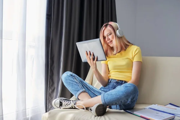 Studentessa adolescente in cuffia in cerca di tablet digitale, seduta a casa sul divano — Foto Stock