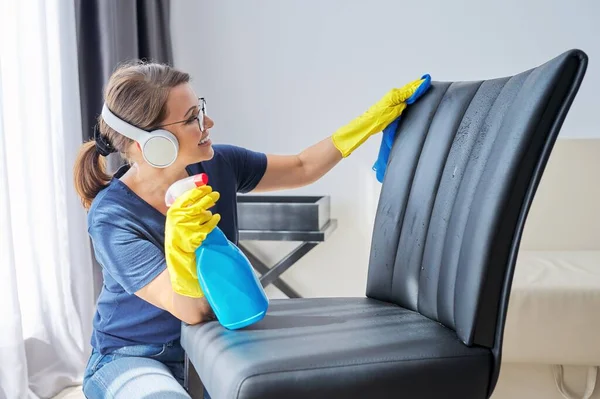 Hausreinigung positiv, Frau mit Kopfhörer und Handschuhen reinigt Sessel, Möbel — Stockfoto