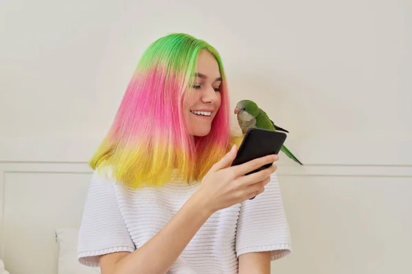Trendy teen girl with smartphone and quaker parrot on her shoulder
