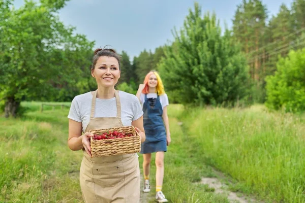 Mor och dotter tonåring går tillsammans med korg med färska jordgubbar — Stockfoto