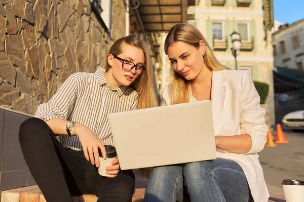 Due giovani donne sorridenti che guardano il monitor del computer portatile, sedute all'aperto — Foto Stock