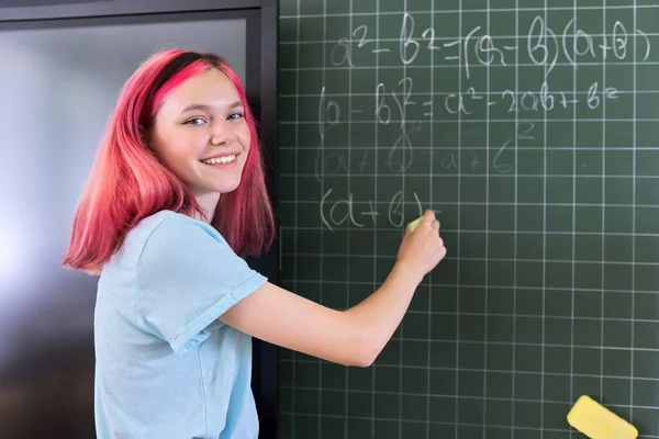 Adolescente estudiante en una lección de matemáticas escribiendo con tiza en una pizarra — Foto de Stock