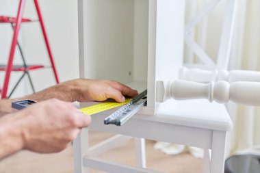 Evdeki ahşap beyaz komodinin montajı, bir işçinin eli kapalı.