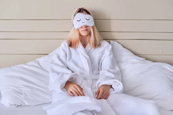 Молода жінка в білому ліжку в халаті, маска для очей — стокове фото