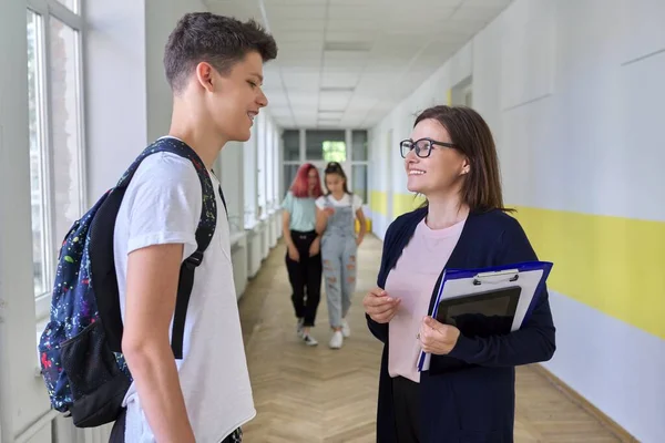 School, college, female teacher talking to a male teenage student in school corridor