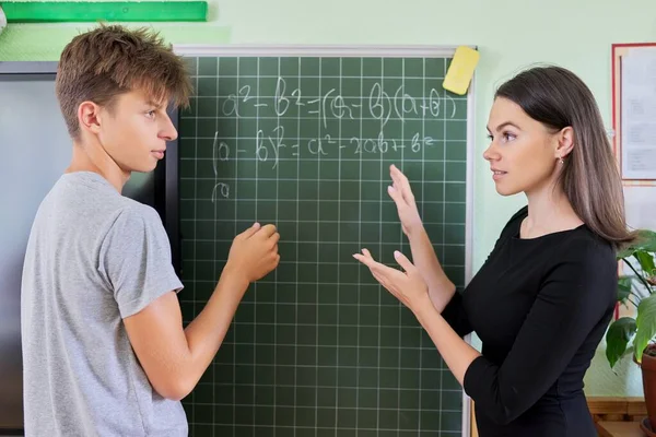 Étudiant adolescent avec professeur près du tableau de craie de l'école à la leçon de mathématiques — Photo