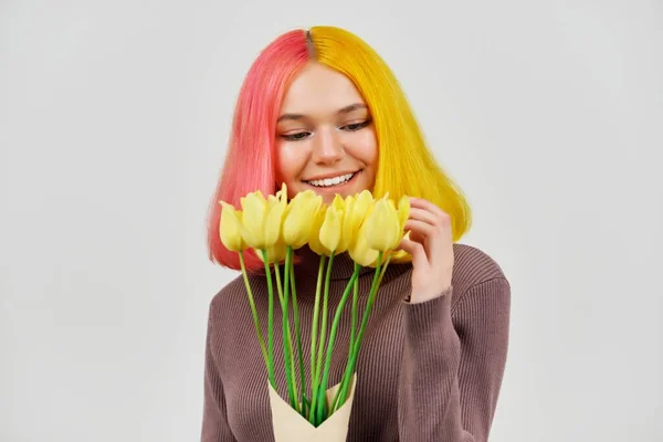 Glad leende tonåring flicka med bukett gula tulpaner på ljus bakgrund — Stockfoto