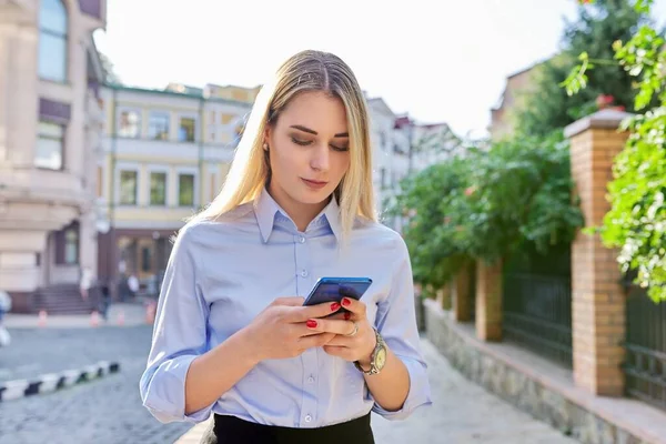 Красивая молодая женщина со смартфоном набирает текст, городской фон — стоковое фото