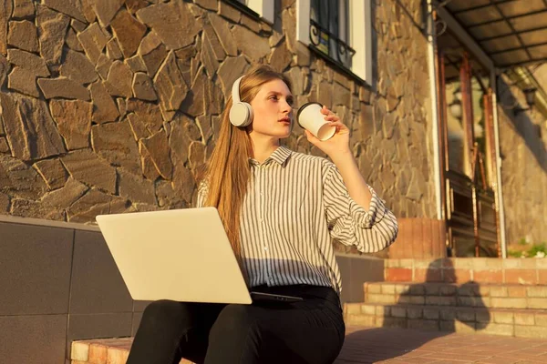 Νεαρή όμορφη γυναίκα σε ακουστικά με φορητό υπολογιστή κάθεται στα σκαλιά εξωτερική — Φωτογραφία Αρχείου