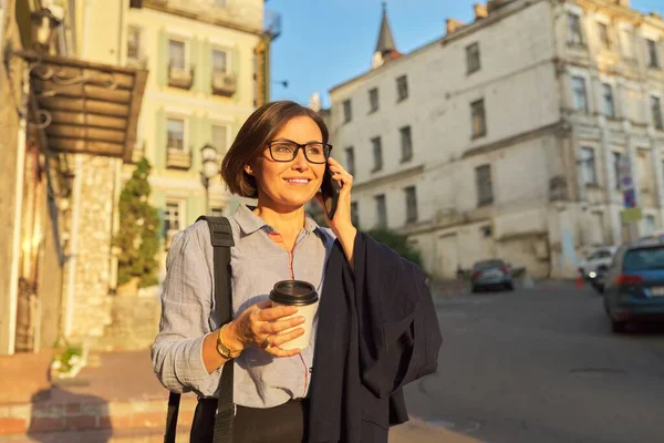 Empresária madura feliz em óculos com xícara de café com smartphone na rua da cidade — Fotografia de Stock