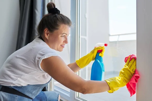 Úklid domu, zralá žena v gumových rukavicích v zástěře mytí oken — Stock fotografie
