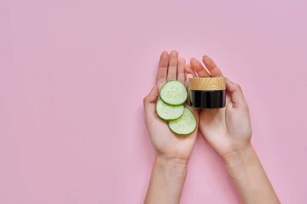 Vrouwen handen met glazen fles, komkommer plakjes op roze achtergrond — Stockfoto