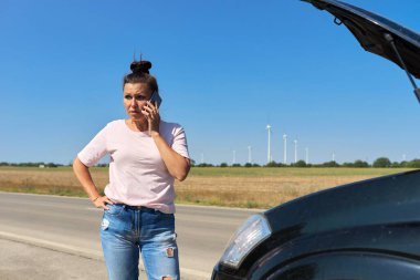 Olgun üzgün kadın sürücü yardım için cep telefonundan arıyor, bir kadın bozuk arabanın yanında.