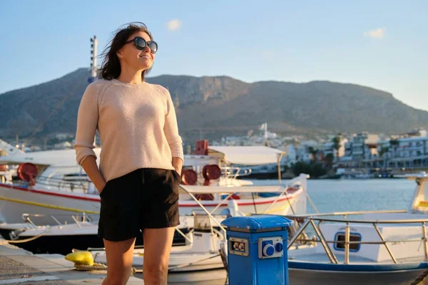 Зріла красива щаслива жінка в сонцезахисних окулярах, що йдуть уздовж морського причалу — стокове фото