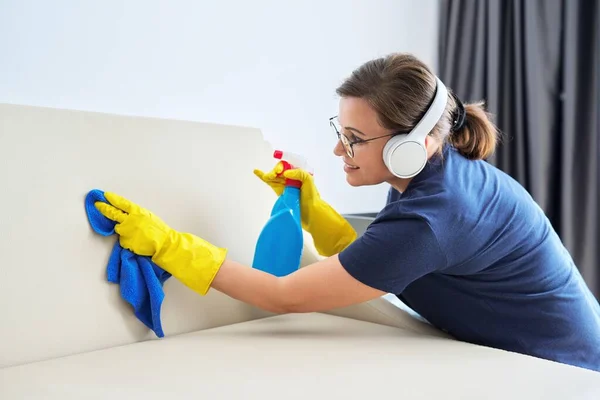 Mujer haciendo limpieza de la casa, hembra en auriculares y guantes con detergente —  Fotos de Stock