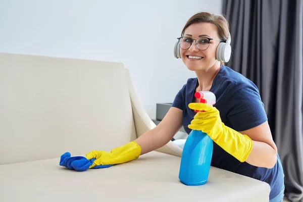 Женщина, убирающая дом, женщина в наушниках и перчатках с моющим средством — стоковое фото