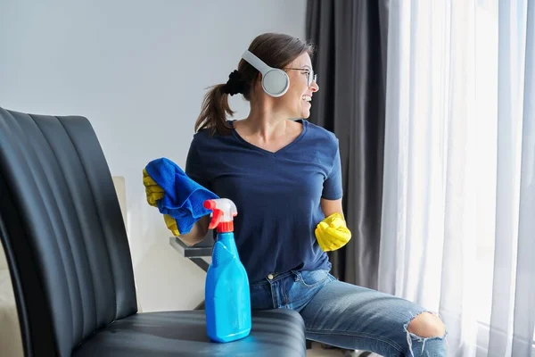 Mujer haciendo limpieza de la casa, hembra en auriculares y guantes con detergente — Foto de Stock