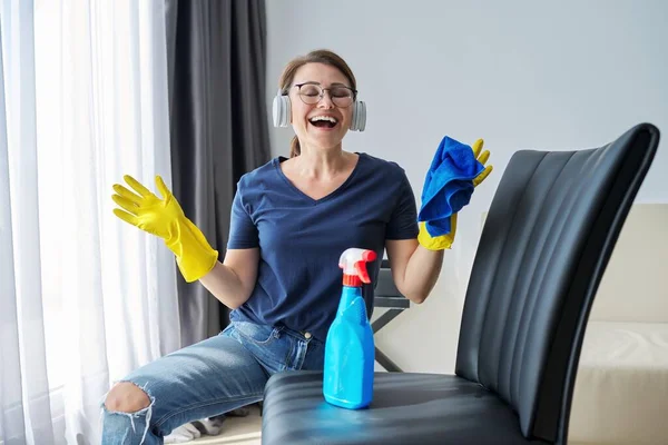 Vrouw doet huisreiniging, vrouw in hoofdtelefoon en handschoenen met wasmiddel — Stockfoto