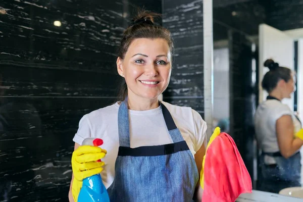 Портрет позитивної жінки середнього віку в фартухах робить прибирання вдома — стокове фото
