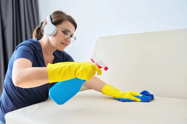 Жінка робить прибирання будинку, жінка в навушниках і рукавичках з миючим засобом — стокове фото