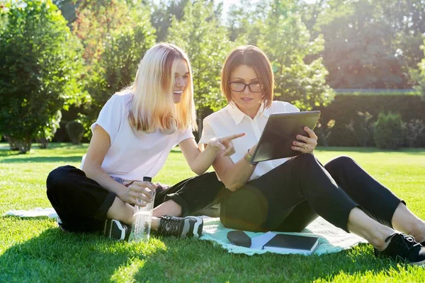 Mulher professora falando com adolescente estudante menina sentado na grama — Fotografia de Stock