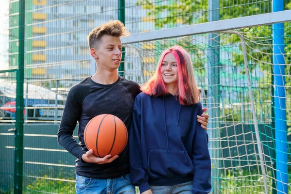 Portrait of guy and teenage girl hugging on basketball court with ball in their hands — Stock Photo, Image