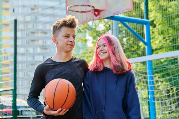 Portrait of guy and teenage girl hugging on basketball court with ball in their hands