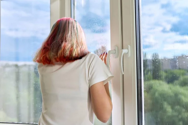 Achteraanzicht van jonge vrouw die naar buiten kijkt regenachtig zomerraam — Stockfoto