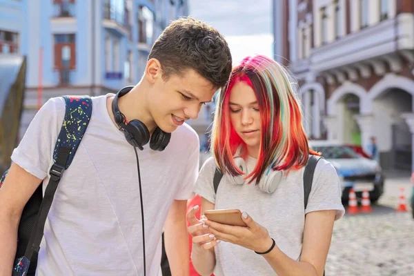 Adolescentes estudiantes chico y chica mirar en la pantalla del teléfono inteligente —  Fotos de Stock