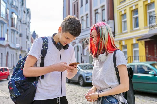 Couple of trending teenagers friends with smartphone on city street