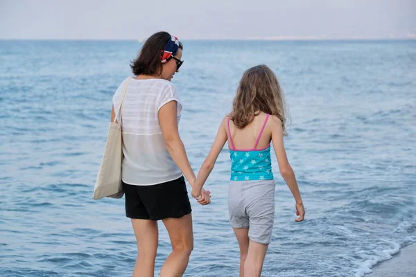 Счастливая мама и дочь, вместе гуляющие по пляжу, держась за руки — стоковое фото