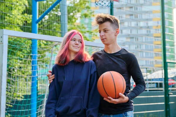 Portrait of guy and teenage girl hugging on basketball court with ball in their hands — Stock Photo, Image