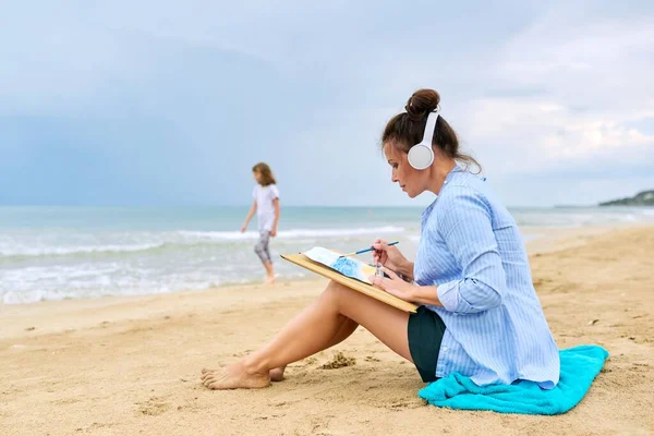 Mujer madura con auriculares escuchando música disfrutando de la pintura acuarela — Foto de Stock