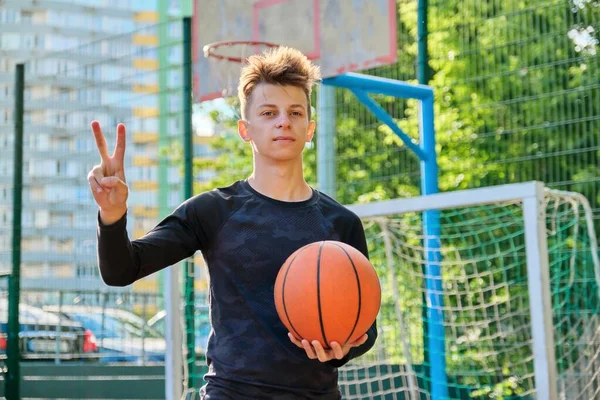 Guy teenager s basketbalovým míč ukazuje vítězství znamení — Stock fotografie