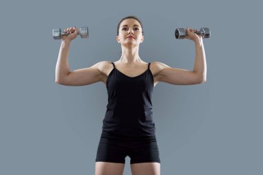 Atletik kaslı genç kadın halterleri kullanarak egzersiz yapıyor.