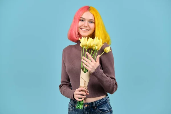 Bellissimo modello adolescente sorridente con bouquet di tulipani gialli su sfondo blu — Foto Stock