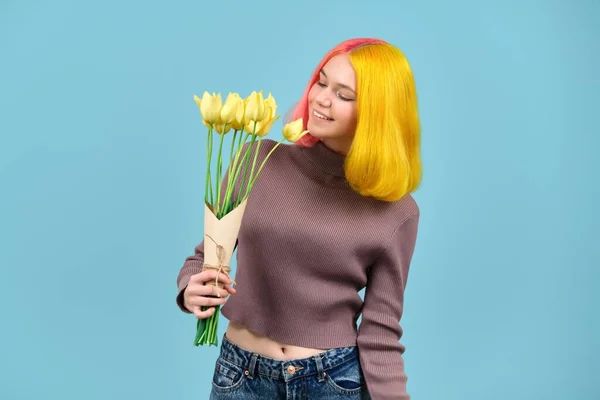 Vacker leende tonåring modell med bukett av gula tulpaner på blå bakgrund — Stockfoto