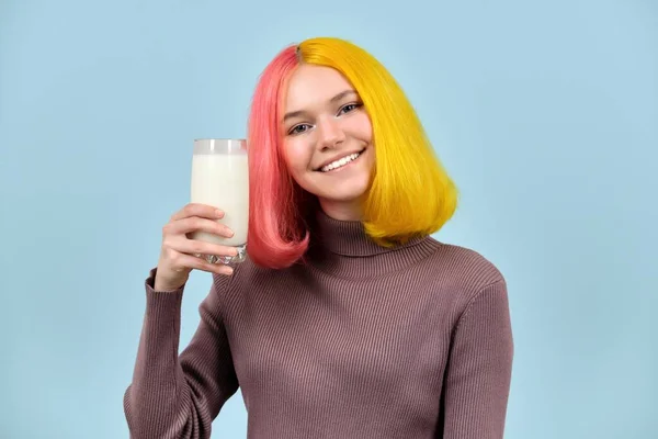 Glas av mjölk i handen av vackra leende tonåring modell, på blå studio bakgrund — Stockfoto