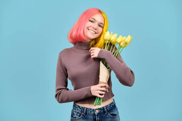 โมเดลวัยรุ่นที่ยิ้มสวยพร้อมช่อดอกทิวลิปสีเหลืองบนพื้นหลังสีฟ้า — ภาพถ่ายสต็อก