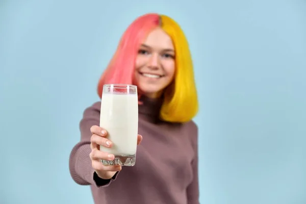 Glas av mjölk i handen av vackra leende tonåring modell, på blå studio bakgrund — Stockfoto