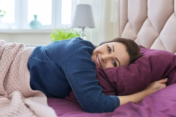 Happy uśmiechnięta dojrzała kobieta leżąca w domu na łóżku z poduszką i kocem odpoczynku — Zdjęcie stockowe