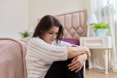 Üzgün, hayal kırıklığına uğramış, depresyonda olan olgun bir kadın evde yerde oturuyor.