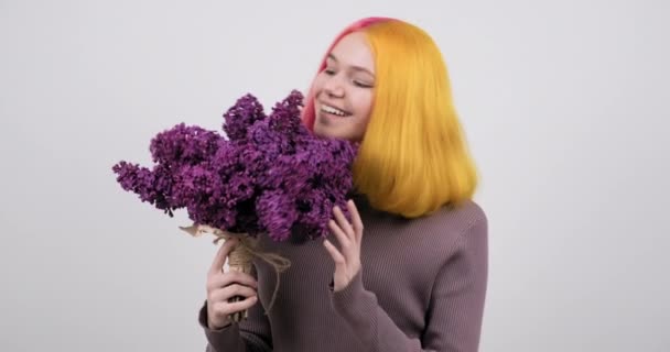 Chica adolescente con el pelo teñido de color amarillo púrpura sosteniendo flores de color lila en las manos — Vídeos de Stock