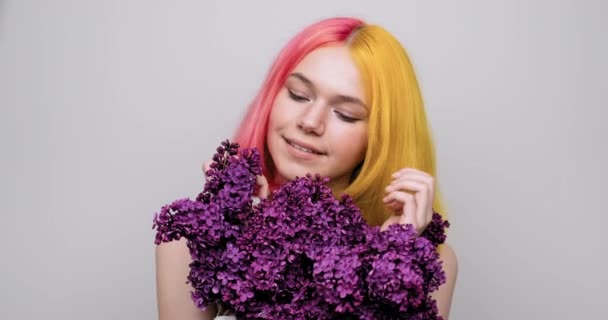 Chica adolescente con el pelo teñido de color amarillo púrpura sosteniendo flores de color lila en las manos — Vídeo de stock