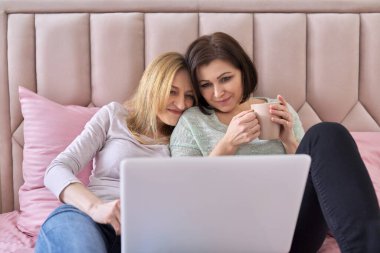 İki orta yaşlı kadın evde dizüstü bilgisayarlarıyla yatıyorlar.