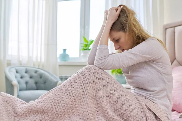 Sad stressful middle-aged woman sitting at home in bed under blanket