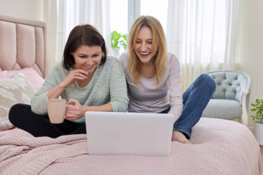 İki orta yaşlı kadın evde dizüstü bilgisayarlarıyla yatıyorlar.