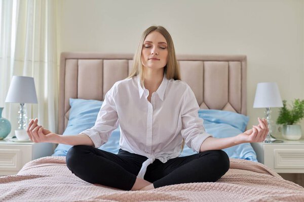 Йога медитация, молодая красивая блондинка сидит в позе лотоса в постели