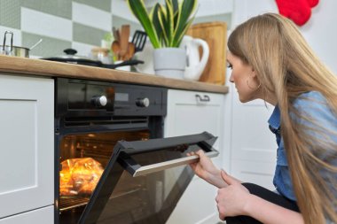 Genç bir kadın fırında salamura edilmiş tavuk pişiriyor.